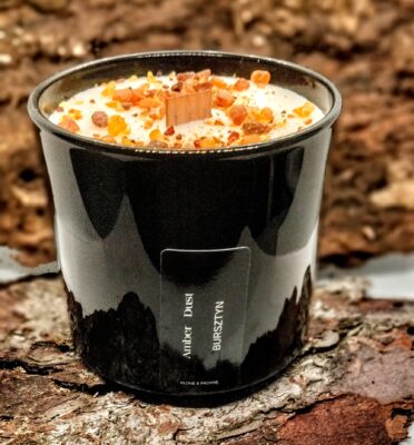 Świeca AmberDust z bursztynem w czarnym pojemniku na tle drewnianej kory